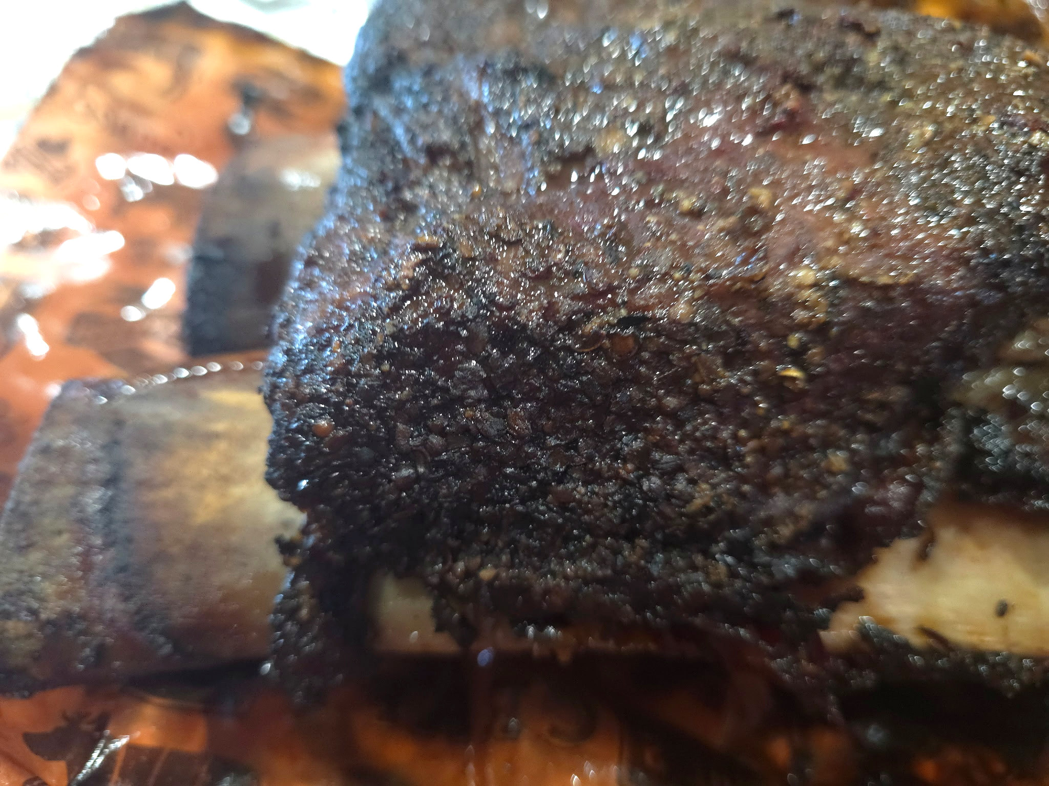 Close-up photograph of the smoky dark bark on a beef rib.