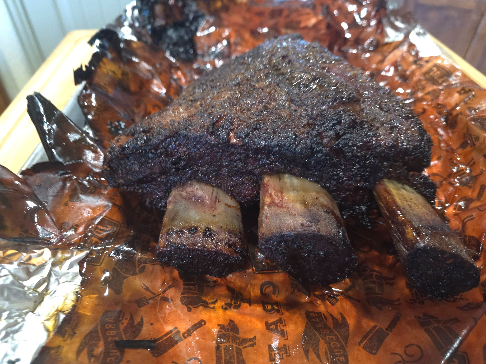 Large, slow-smoked beef ribs with dark seasoned bark and visible bones on the pitmaster's work surface.