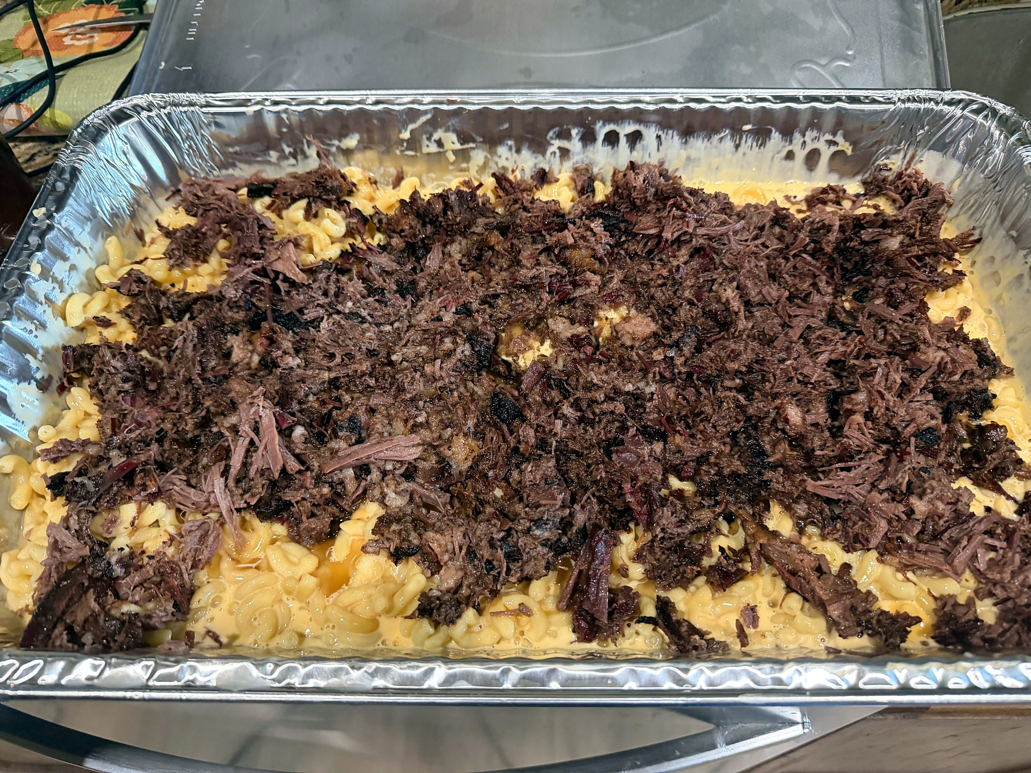 Pan of mac and cheese topped with shredded smoked brisket.