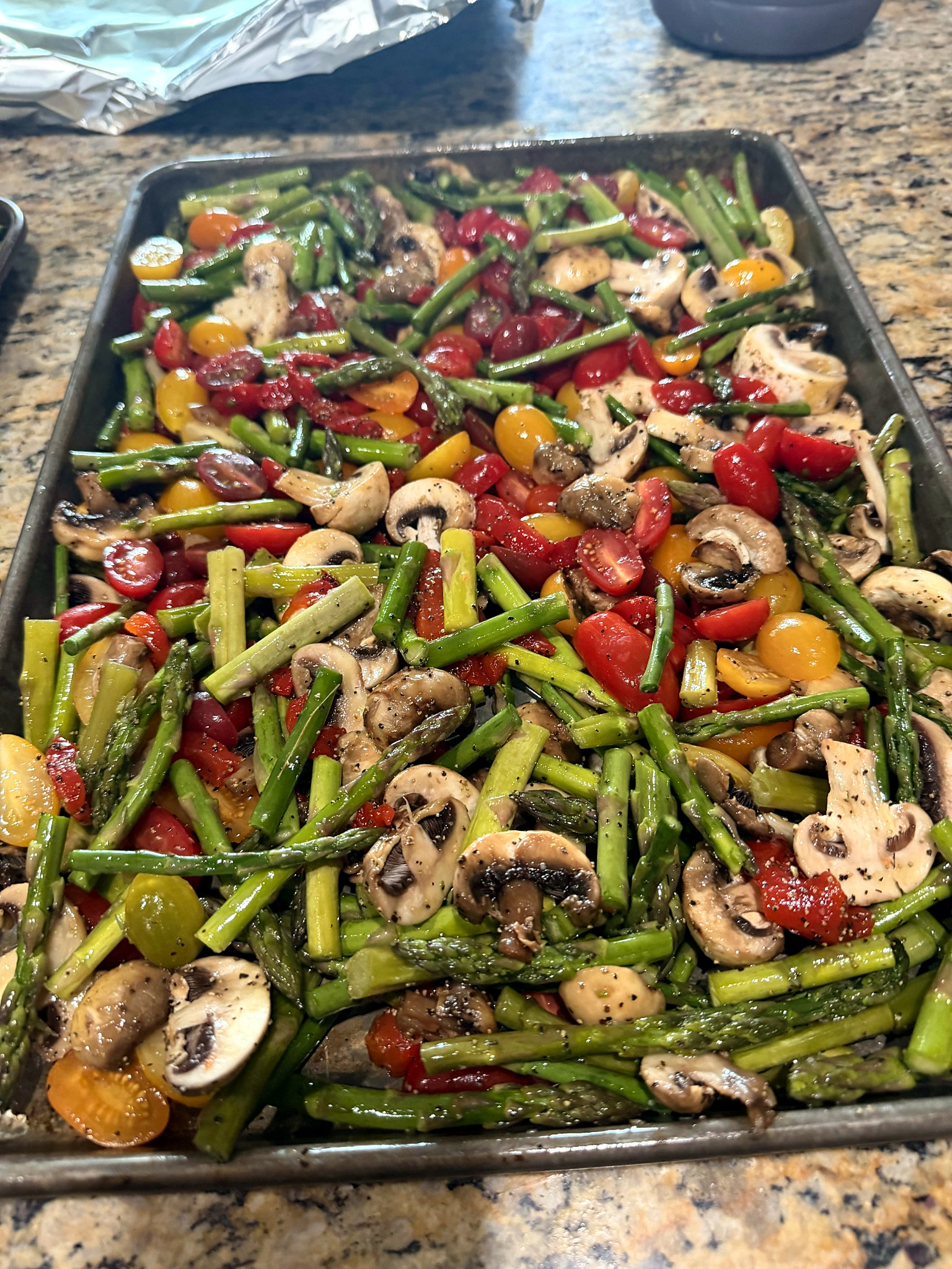Catering tray of mixed vegetables with asparagus, mushrooms, and red and yellow cherry tomatoes.
