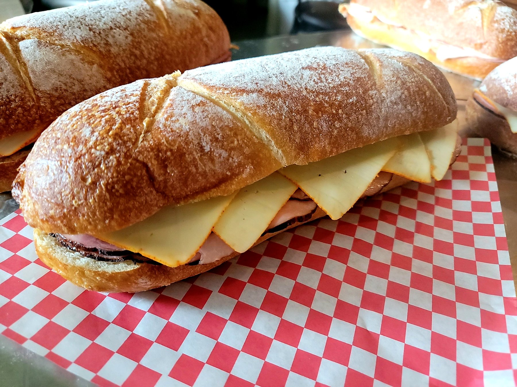 Catered sandwiches with sliced meat and cheese on crusty bread over red checkered deli paper.